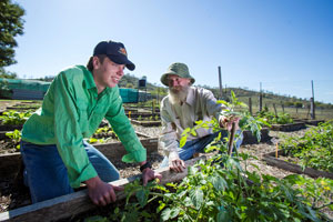 Student and teacher kneeling next to garden bed with bright green vegetation.