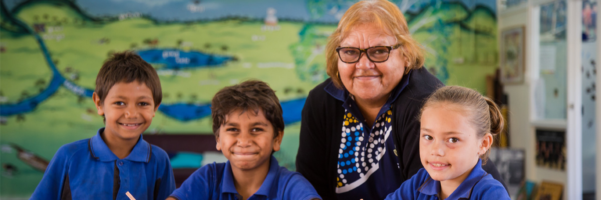 Smiling teacher with three primary school students in a classroom.