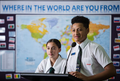 Two students standing in front of a notice board. Text says, Every culturally and linguistically diverse student succeeding.